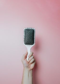 Minimal image of a hand holding an hair comb over a light color background, copy space, minimal image. Hair styling concept, beauty styling
