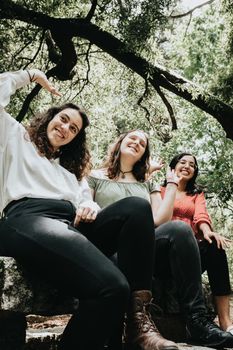 Three young woman saluting someone off camera in the forest, multicultural friendship concept, happiness concept