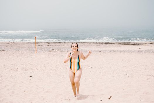 Young lady running and having fun at the beach enjoying warm, tropical ocean water, colorful swimsuit, bright day ocean