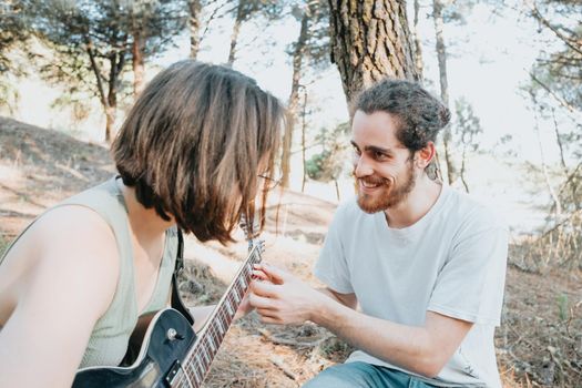 Handsome Young Man Teaching hipster Girl to Play Guitar on the forest trees during a sunset. Learning a new skill joyful concept. Music with copy space. Young couple electric guitar