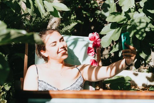 Young woman taking a selfie while relaxing on a garden during a super sunny day, social network concept, happy girl