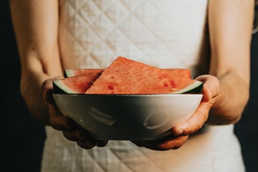 Old waitress offers and holds a watermelon in a dish, fruits, healthy life, good eating, mediterranean concepts, copy space, vertical image, summer eating, and refreshing fruits
