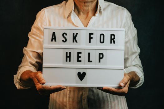 Old woman holding a sign that says ask for help, while smiling to camera, mental health and depression support concepts