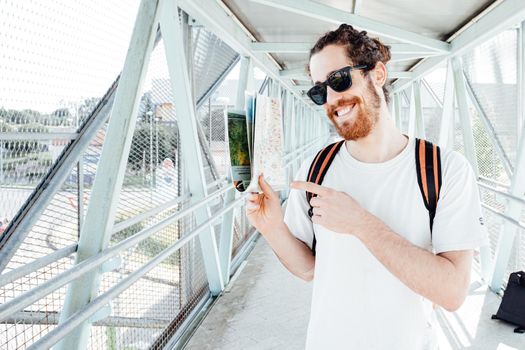 Portrait of a young man at the airport or bus station , luggage, bags and suitcase holding map. Smiling hipster traveler with sunglasses, copy space, sunny day