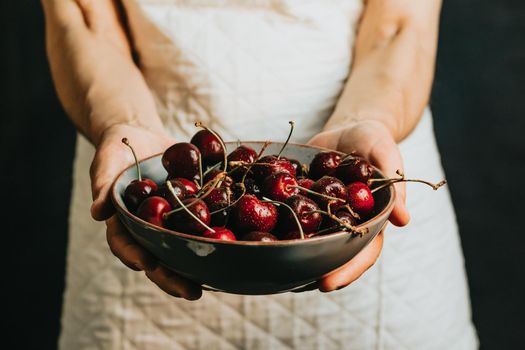 Old waitress offers and holds a bunch of cherry in a dish, fruits, healthy life, good eating, mediterranean concepts, copy space, vertical image