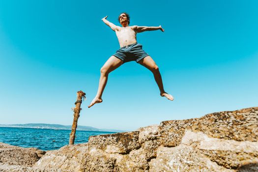Young male with long hair jumping in the air, shirtless during a sunny day, space and liberty concept, holidays, fantastic image, beach day