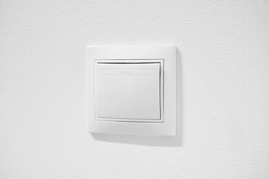 Inexpensive plastic push button switch against white wall. White common toggle switch in home. Cheap simple single-pole light switch. Standart rocker switch for exhaust fan or lighting applications