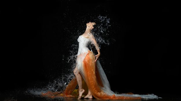 beautiful woman of Caucasian appearance with black hair dances in drops of water on a black background. Woman wearing white corset and skirt