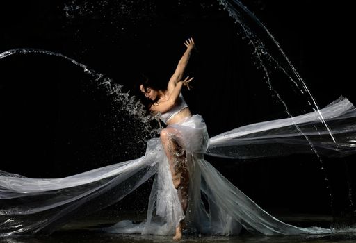young beautiful woman of Caucasian appearance with long hair dances in drops of water on a black background