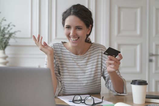 Young smiling italian woman making payment with plastic card during online shopping on laptop