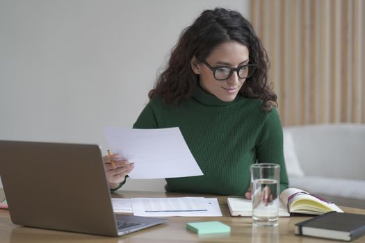 Young pleasant Italian female in glasses preparing report while working on laptop in modern office