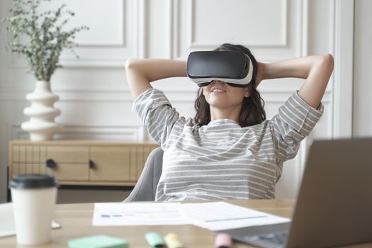 Relaxed young woman office worker in VR headset or helmet watching in 360 degrees video or movie