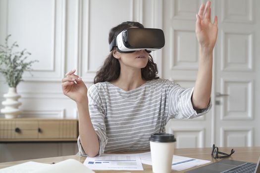 Concentrated woman bank accountant in VR headset sitting at desk at home office