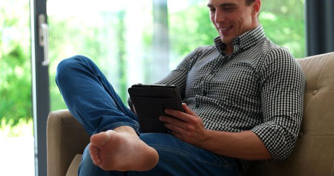 Man is Laying on Couch at Home and Using Tablet