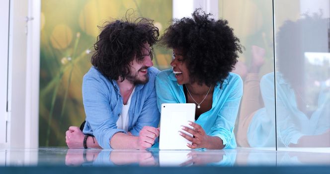 Happy young multiethnic couple lying on floor having fun using Digital Tablet