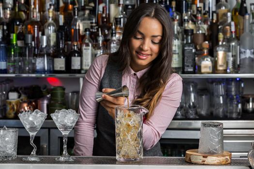 Positive female barkeeper making cocktail in bar