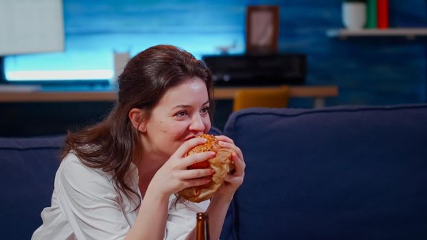 Young person laughing at TV while eating hamburger