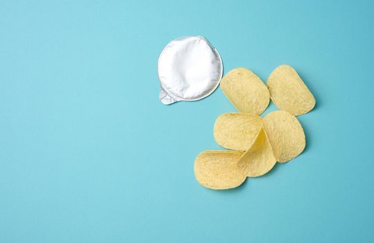 round potato chips and foil lid on blue background, top view