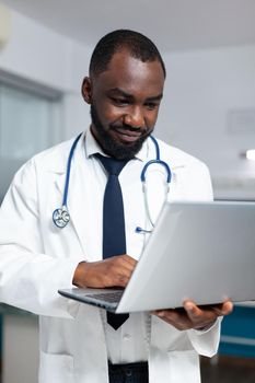African american practitioner doctor typing medical expertise on laptop