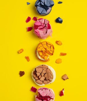 broken round macarons with crumbs on a yellow background, delicious dessert, top view