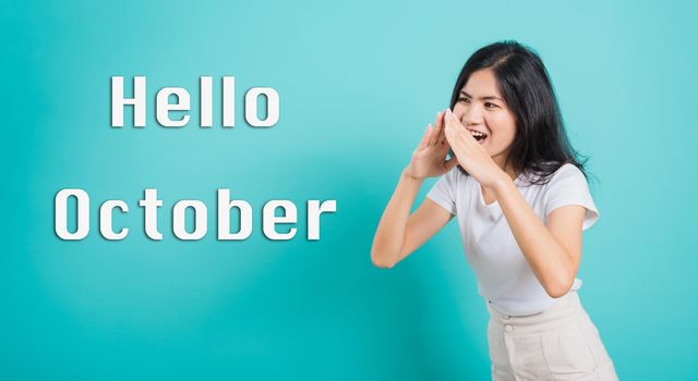 Hello October, Portrait Asian beautiful happy young woman smile white teeth wear white t-shirt standing shouting with hands cover mouth, studio shot isolated on a blue background