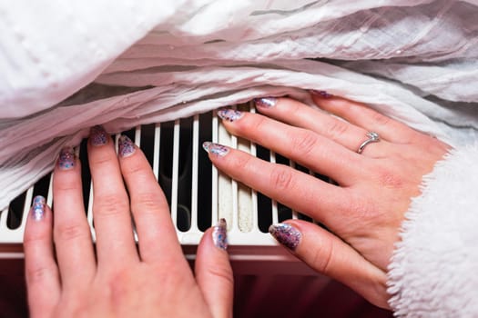Woman warming up her hands on a white radiator