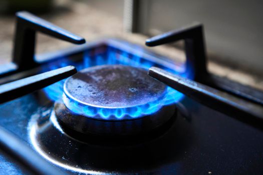Cooker as heater. Wastage of natural resources. Blue flame from gas hob produce greenhouse gas emissions. Kitchen stove grate on a burner fuelled by combustible natural gas or syngas, propane, butane.