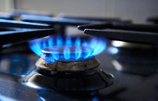 Kitchen stove grate on a burner fuelled by combustible natural gas or syngas, propane, butane. Cooker as heater. Wastage of natural resources. Blue flame from gas hob produce greenhouse gas emissions