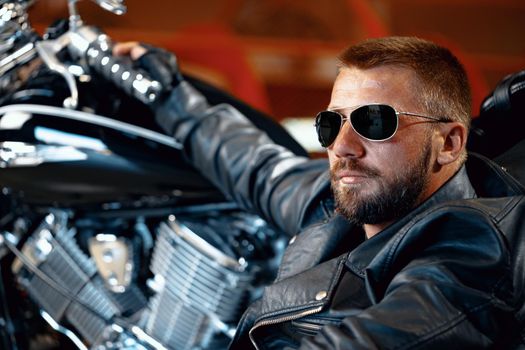 Cool man biker in sunglasses sitting near his motocycle