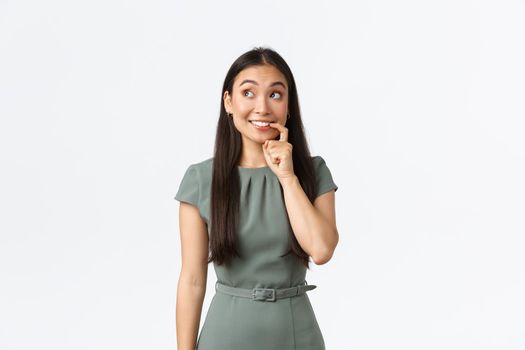 Small business owners, women entrepreneurs concept. Tempting and excited cute asian woman biting finger and looking with desire, thinking, making decision, standing white background