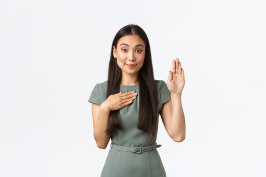 Small business owners, women entrepreneurs concept. Honest pretty asian female making oath, businesswoman raise one hand and hold another on heart as making promise, telling truth