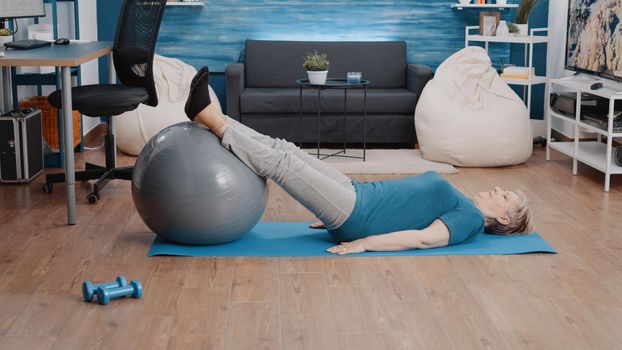 Woman using fitness toning ball to train leg muscles on mat
