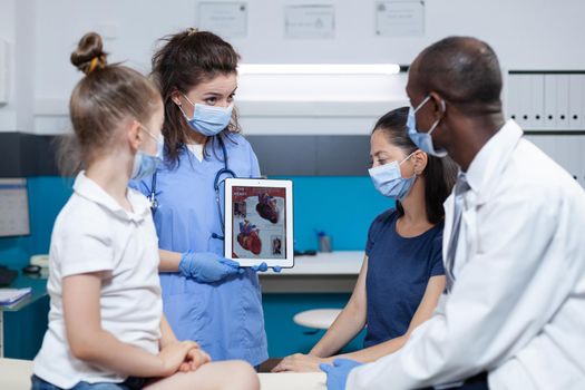 Medical asisstant holding tablet with heart expertise on screen during clinical appointment