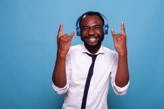 Smiling man full of energy doing rock and roll hand sign while listening to music