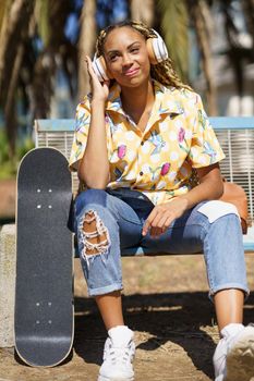 African woman with skateboard relaxing after riding skateboard listening to the music