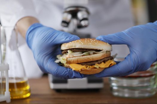 Male chemist holding tasty burger in hand with blue protective glove