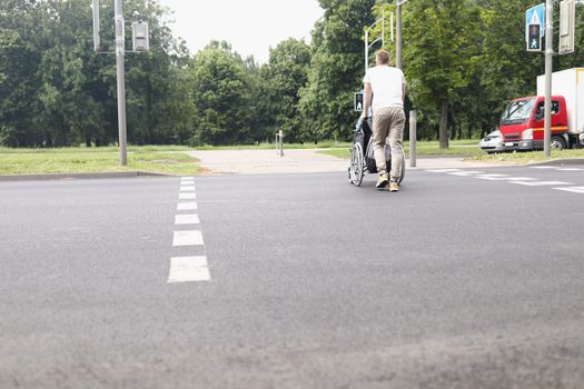 Man drive woman on wheelchair across street at pedestrian crossing
