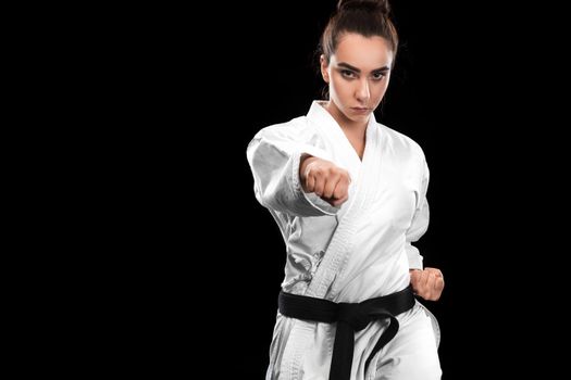 Portrait of sporty karate and taekwondo woman in white kimono with black belt on dark background.
