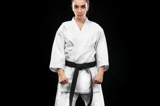Portrait of sporty karate and taekwondo woman in white kimono with black belt on dark background.