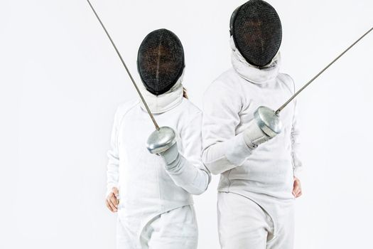 Two Young fencers athletes wearing mask and white fencing costume and holding the sword. Isolated on white background