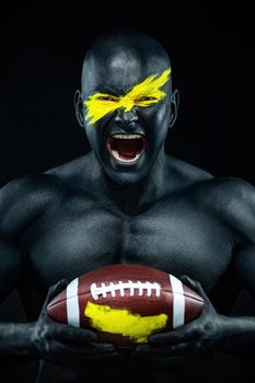 American football fan with ball on black background. Fitness and sport motivation. Strong fit and athletic guy in body paint like a super hero.