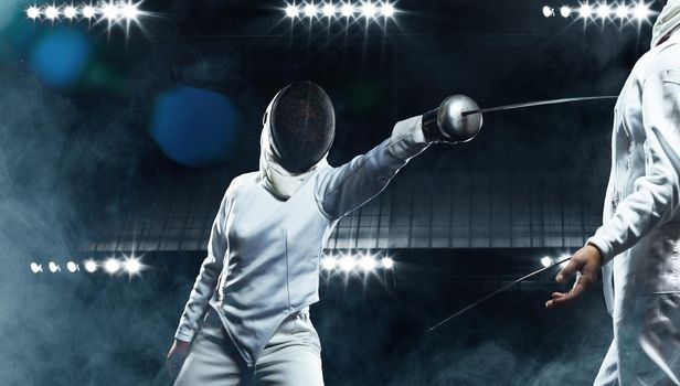 Young fencer athletes wearing mask and white fencing costume. Fight on the sword on black background with lights.