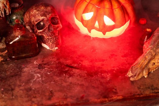 Halloween. Scary Halloween pumpkin with carved face on table in dark room with human skull and animal skull