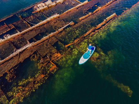 Woman on paddle board, sup next to Abandoned broken shipwreck sticking out of the sea