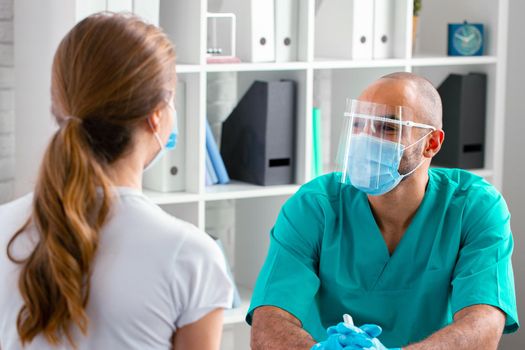 Doctor in face mask talking to female patient in clinic