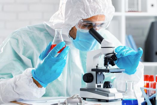 Medical worker in protective gown looking in microscope