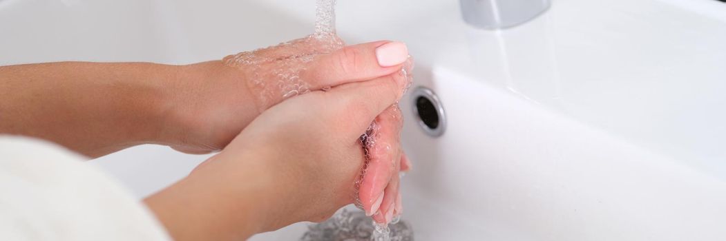 Woman washes hands under running water in sink closeup