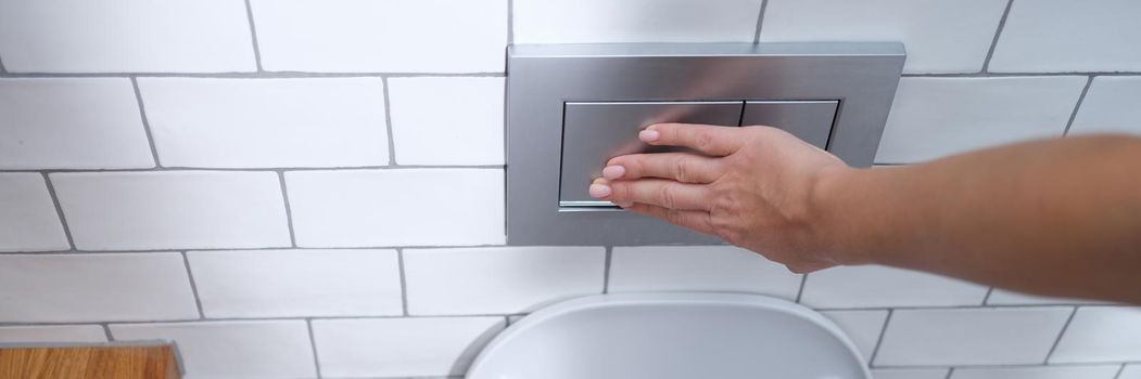 Female hand presses flush button in toilet closeup