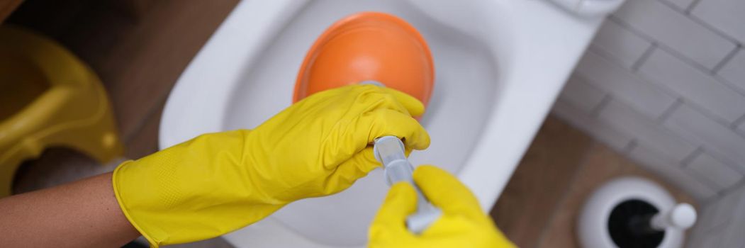 Person in yellow gloves and plunger cleans toilet closeup