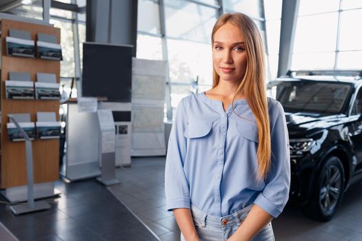 Young beautiful car saleswoman standing in car showroom